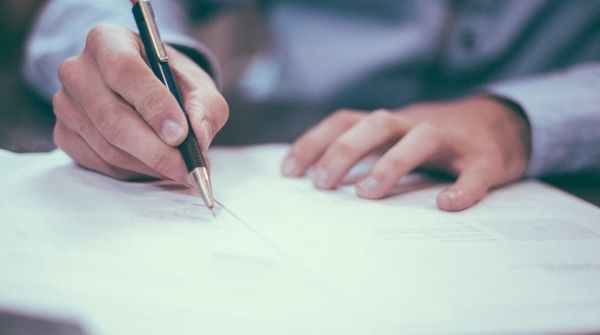 Ein Mann im Anzug unterschreibt verschiedene Dokumente und Referenzen